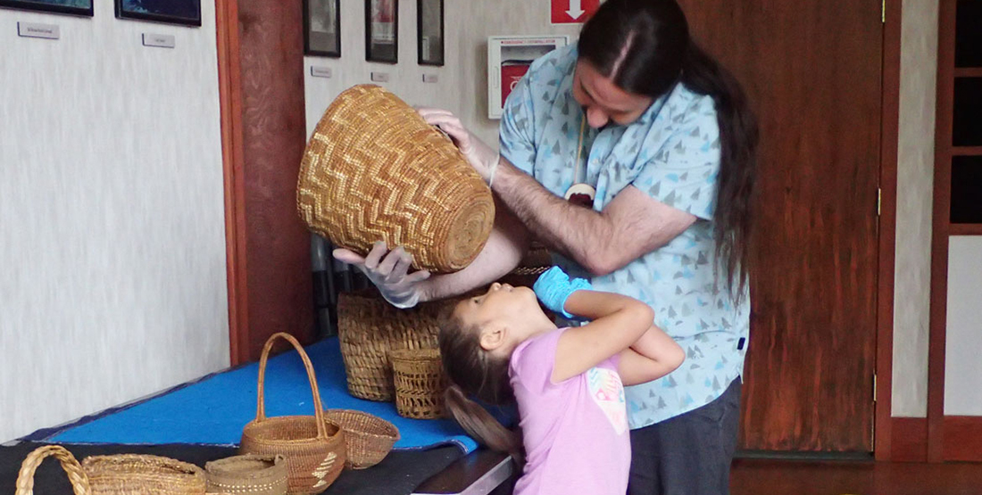A young man holds up a basket as a small child peers at the underside