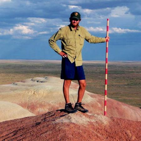 A male researcher stands in the Wyoming desert holding a red and white striped pole