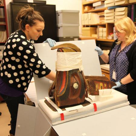 Two woman carefully unpack the native art mask from a box