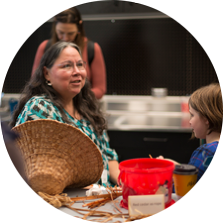 a woman works on a cedar hat as a young girl watches
