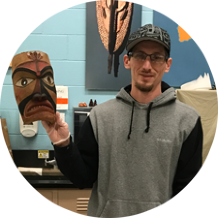 a man stands holding a Native mask in one hand